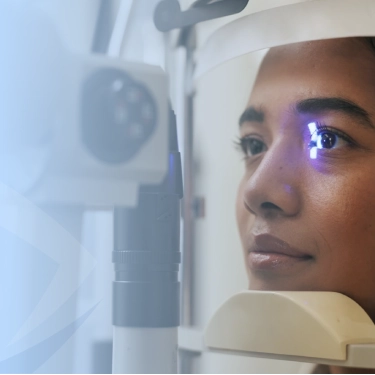 Woman undergoing an eye examination with a slit-lamp; blue light reflects in her eye as a clinician peers through the instrument.